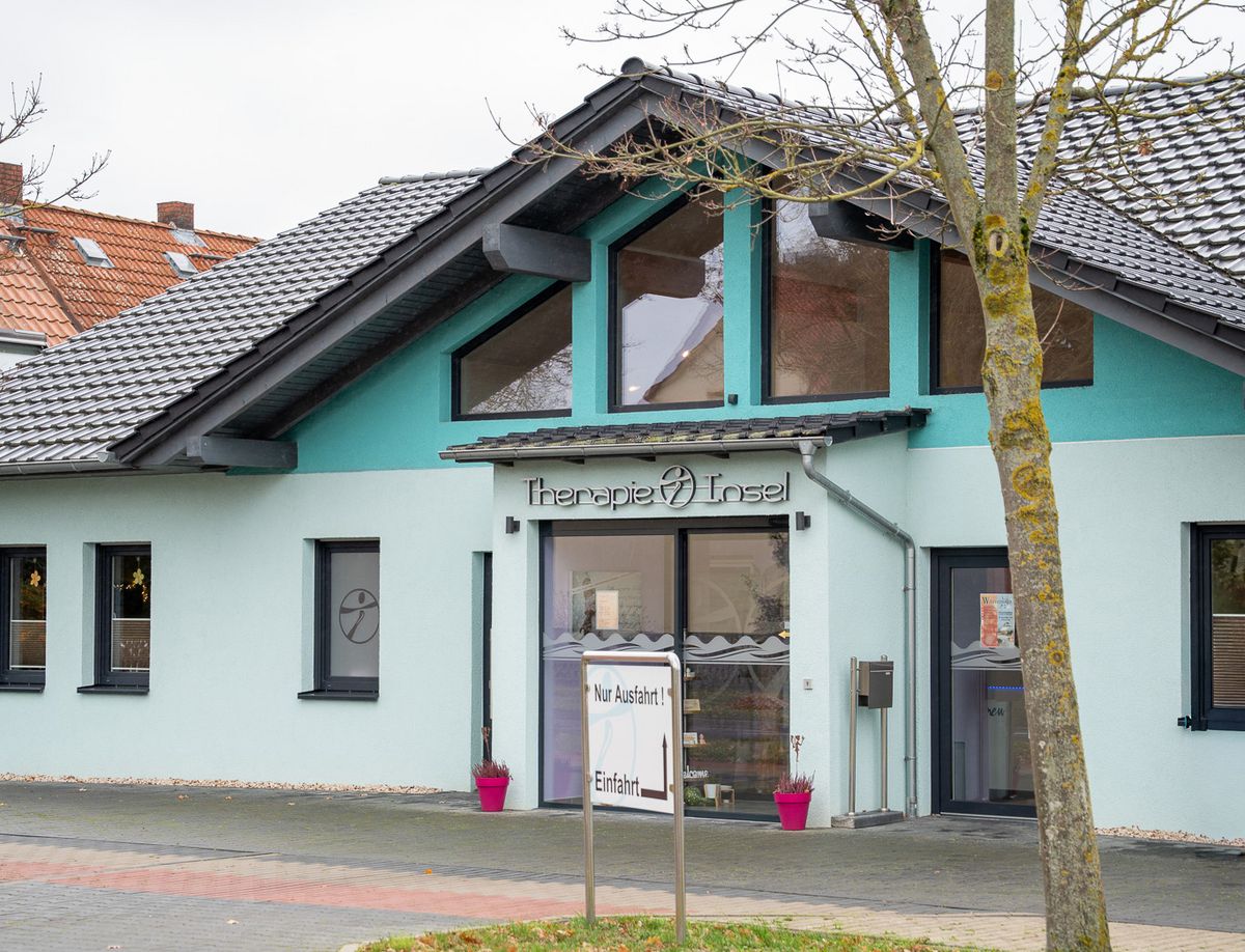 Ein modernes Gebäude mit der Aufschrift "Therapie Insel" steht unter einem bewölkten Himmel.